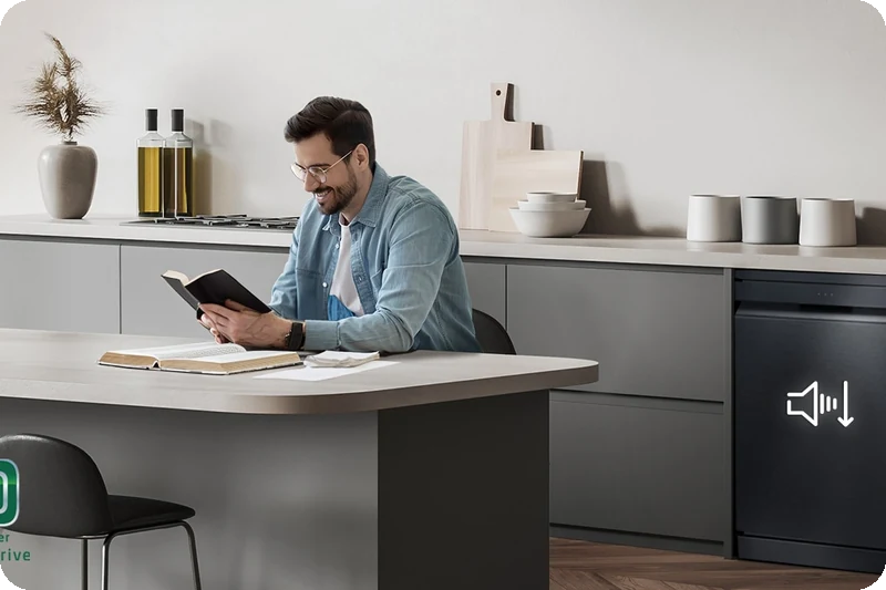 A man reading at the kitchen island while the dishwasher runs quietly in the background.