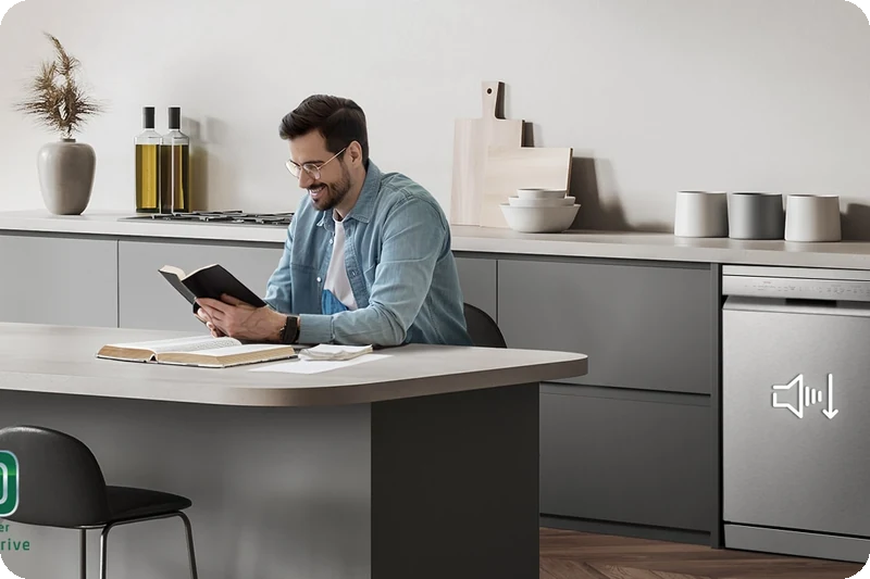 A man reading at the kitchen island while the dishwasher runs quietly in the background.